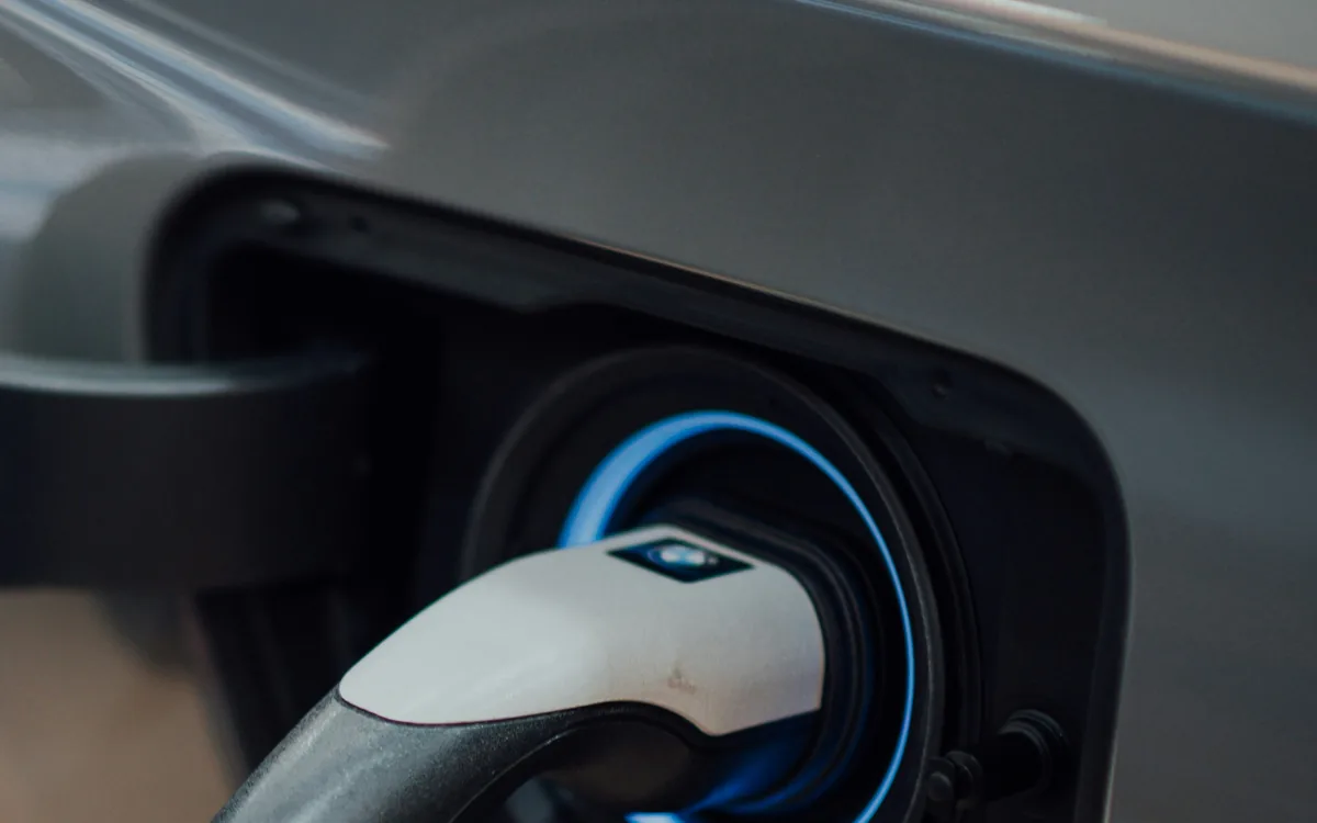 Detalle del conector de recarga enchufado a la toma de un coche eléctrico, con el aro indicador encendido en azul.