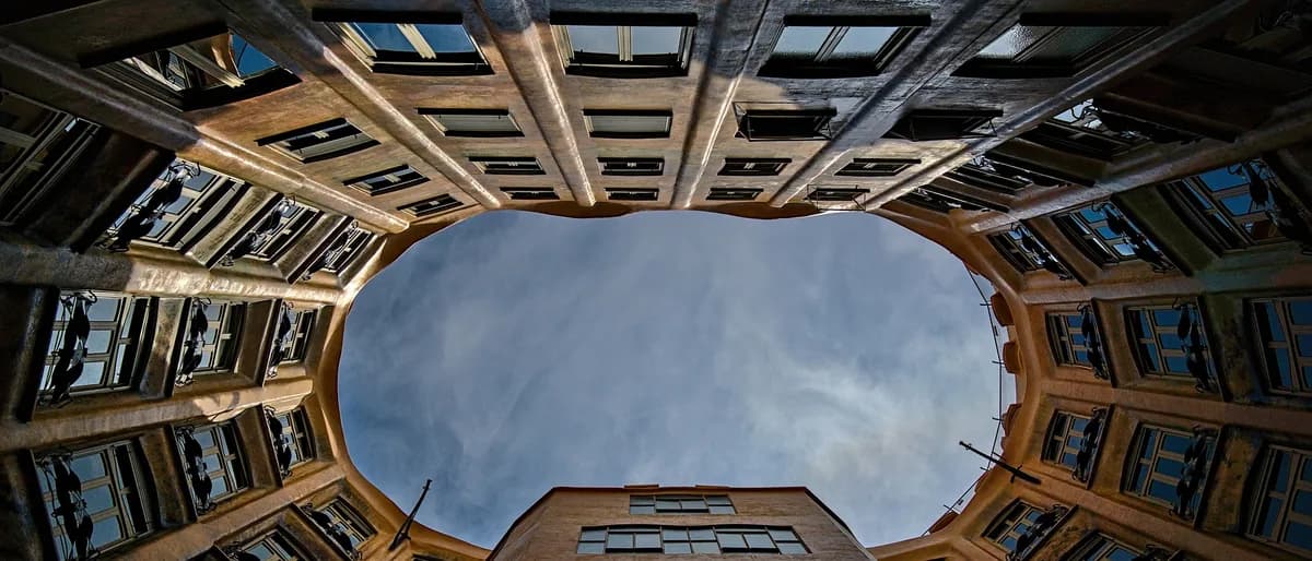 Patio de luces de un edificio de viviendas visto desde abajo, con las galerías y ventanas de los vecinos alrededor del hueco de cielo.