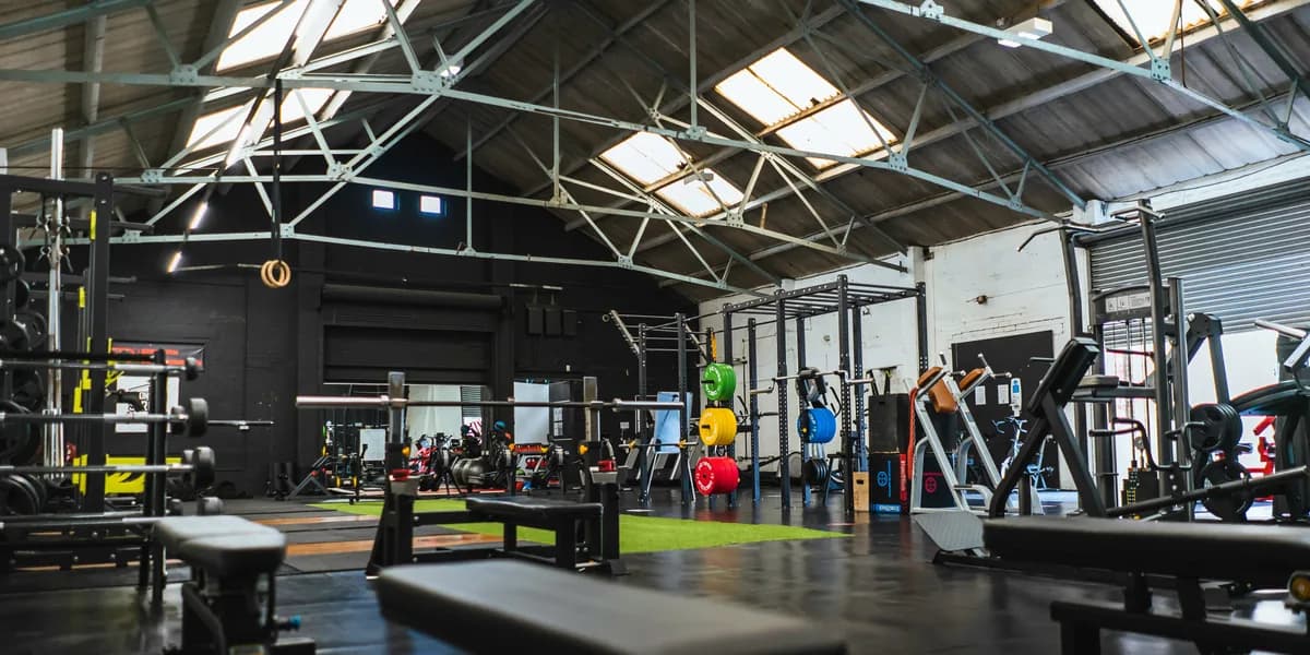 Sala de máquinas de un gimnasio en una nave con cubierta de lucernarios, con bancos y racks de pesas.