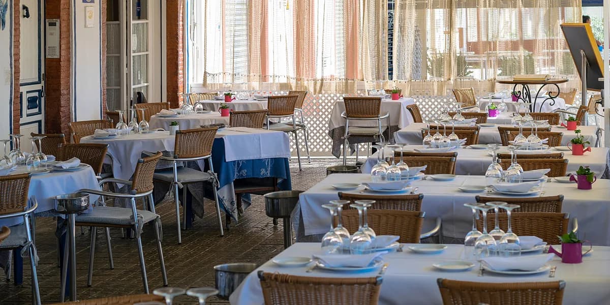 Comedor de un restaurante español con mesas vestidas de blanco, sillas de mimbre y cortinas de red.