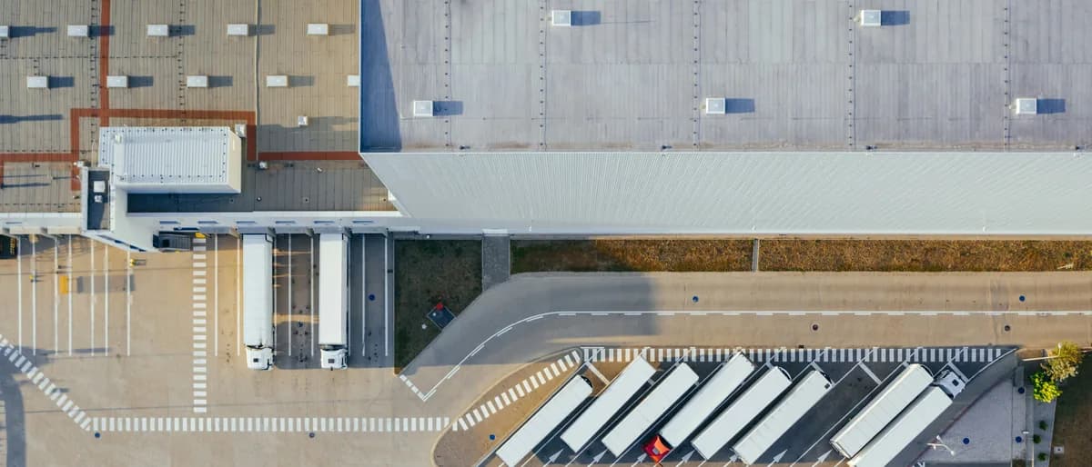 Vista aérea cenital de una nave logística con la cubierta ocupando media imagen y los muelles de carga con camiones estacionados en espina.